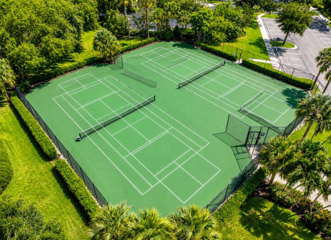 A tennis court surrounded by well-maintained greenery and a parking area.