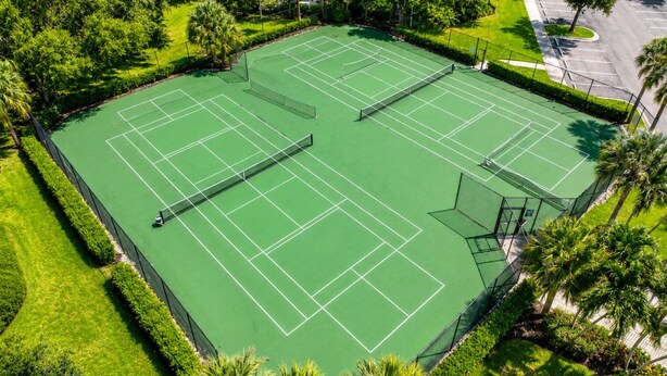 A tennis court surrounded by well-maintained greenery and a parking area. - The Fairway Retreat at GreenLinks (Naples)