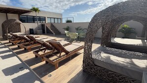 A rooftop lounge area with wooden lounge chairs, a wicker arch, and a view of the building's exterior. - Studio in the heart of Tulum with rooftop pool - Solum Living (Tulum)