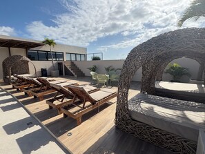Eine Dachterrasse mit Holzliegen, einem Korbschwungstuhl und Blick auf die Außenansicht des Gebäudes.