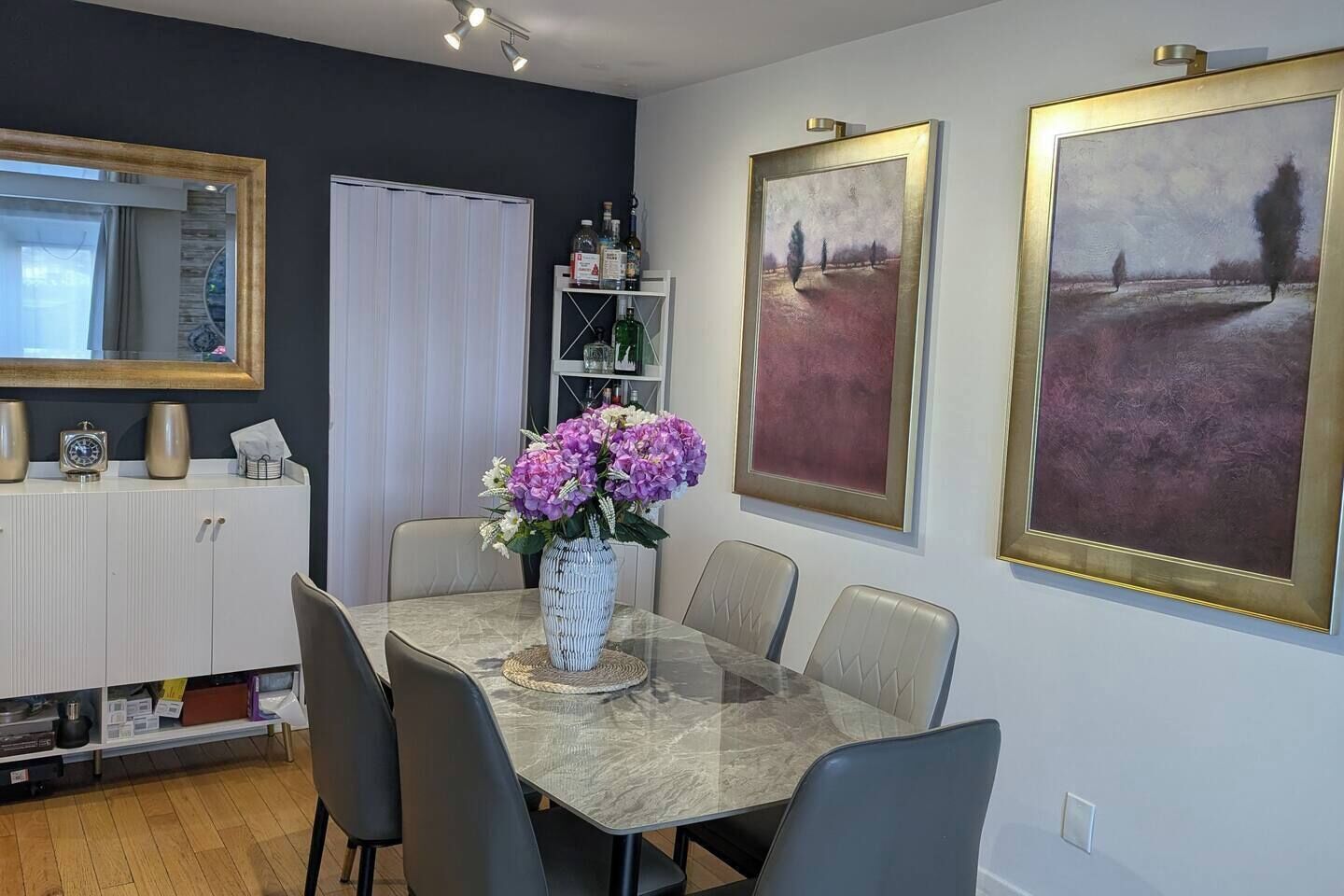 Un comedor con una mesa, sillas, un jarrón de flores y cuadros colgados en la pared.