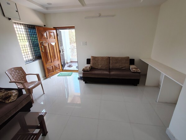 Una sala de estar con sofá, sillón, mesa de vidrio y puerta que da al exterior.