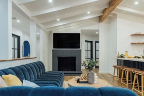 Ein modernes Wohnzimmer mit Kamin, einem blauen Sofa, einem Couchtisch und einer Küchenzeile mit Barhocker.