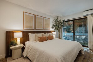 Ein Schlafzimmer mit einem großen Bett, Nachttischlampen, einem Beistelltisch und Blick auf einen Steinhof durch eine Glastür.