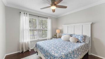 A bedroom with a bed, a ceiling fan, a window with curtains, and a nightstand with a lamp.