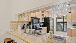 A modern kitchen with a marble countertop, stainless steel appliances, wooden cabinets, and a wine rack.