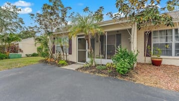 A residential building with a covered porch, a driveway, and various plants.