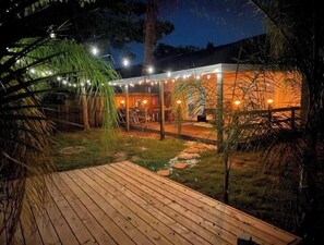 Una terraza de madera que conduce a un espacio exterior cubierto con luces colgantes.