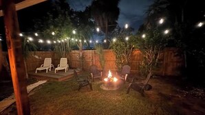 Un espace extérieur aménagé avec une terrasse, un foyer, des fauteuils et des guirlandes lumineuses.