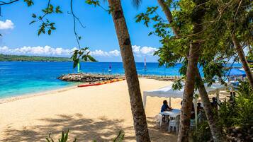 A beach with a clear view of the ocean, a pier with a sailboat, and a white tent with people seated.