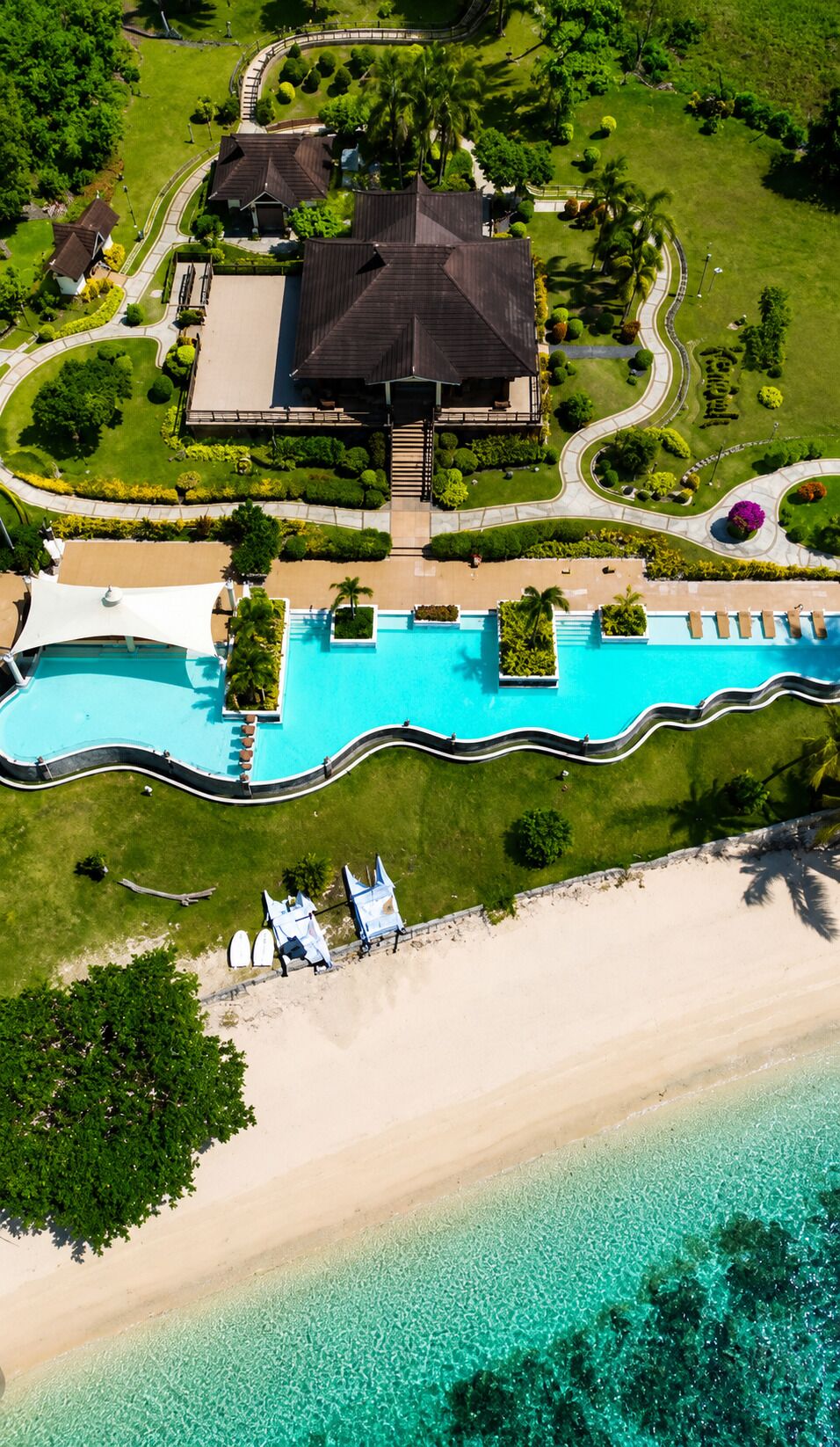 Vue aérienne d’un complexe hôtelier doté d’une piscine, d’un accès à la plage et de jardins aménagés avec soin.