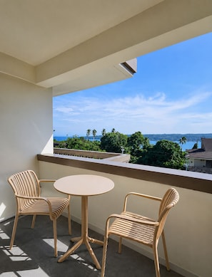 A balcony with two chairs and a small table, overlooking a scenic view of the ocean and palm trees.