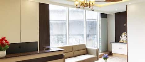 Una sala de estar moderna con un sofá, una mesa de centro y un escritorio con una computadora. Hay un ventanal que ofrece vistas de la ciudad.