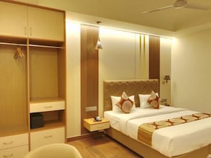 Una habitación de hotel con una cama grande, un armario, una mesita de noche y un ventilador de techo.