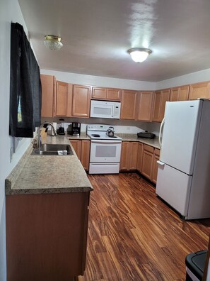 A compact kitchen with wooden cabinets, a white stove, a microwave, and a refrigerator.