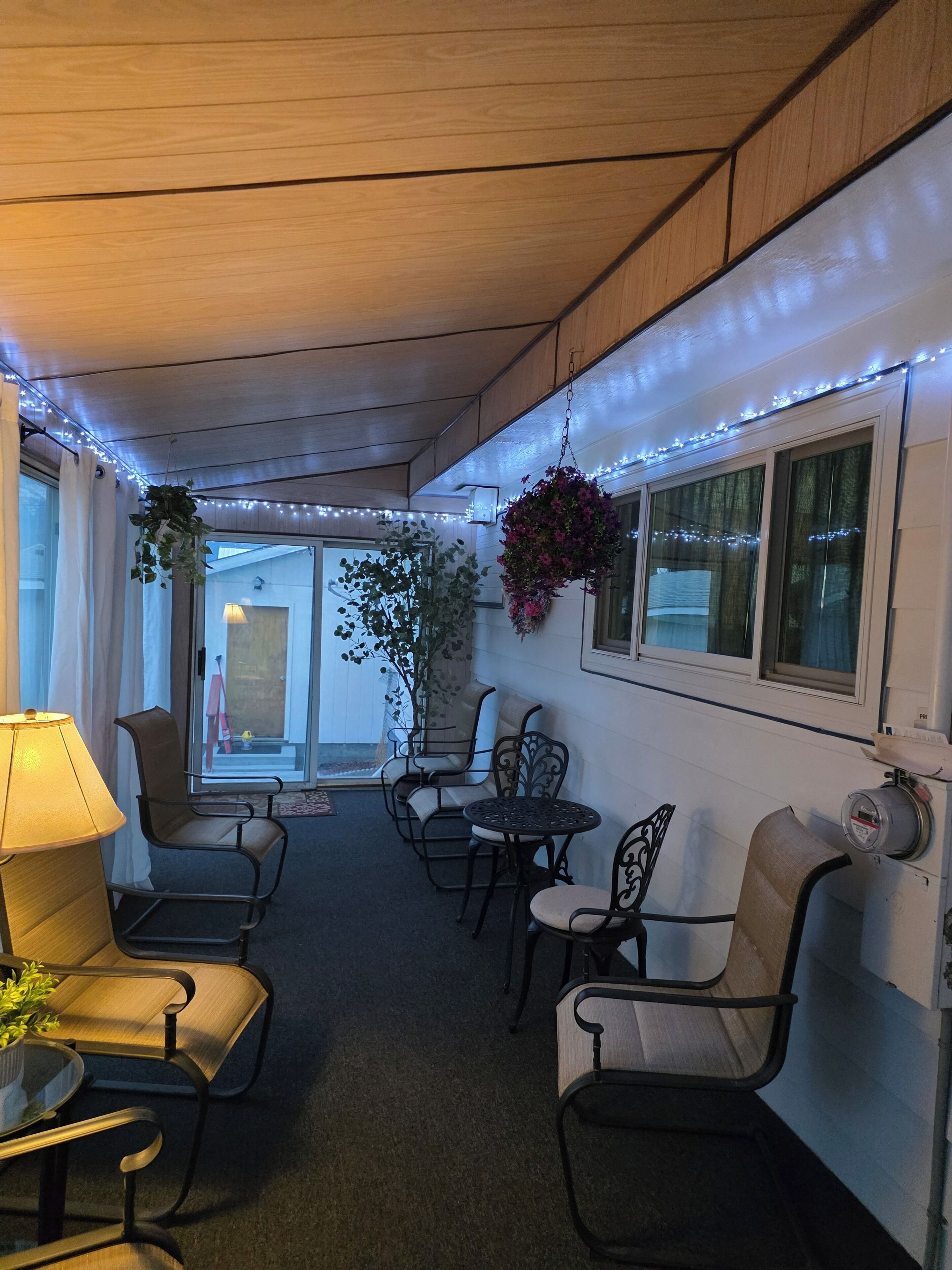A cozy indoor seating area with chairs and a table, a hanging plant, and a window with curtains.