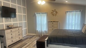 A bedroom with a bed, a dresser, a TV mounted on the wall, and a ceiling fan.