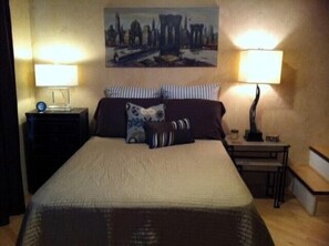 A hotel room with a large bed, two bedside tables, a nightstand, a lamp, and a painting on the wall. - Charming Flat in Fort Worth (Fort Worth)