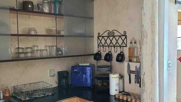 Een keuken met houten kastjes, een zwart aanrecht, een koffiezetapparaat en een prullenbak.