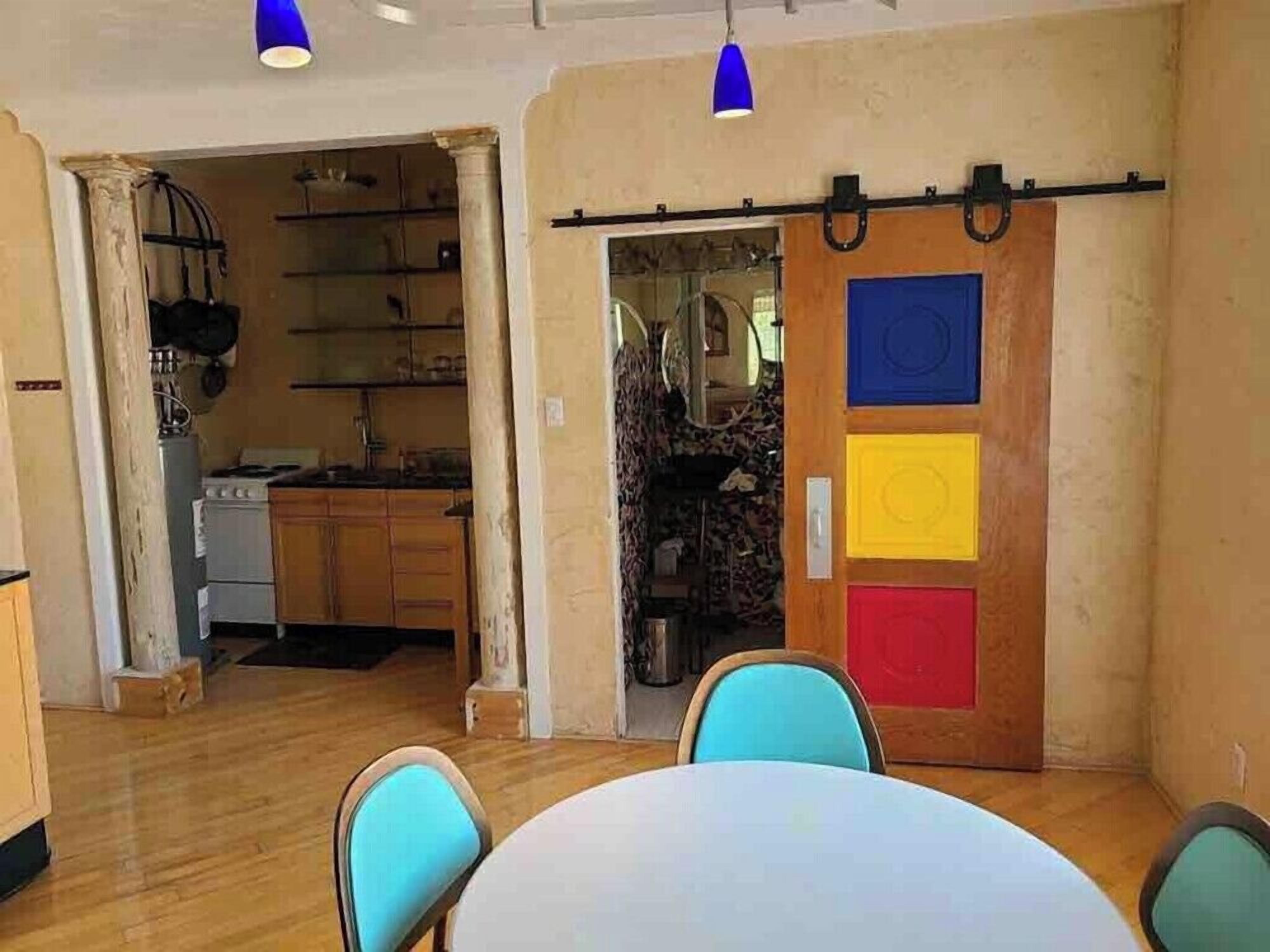 A room with a dining table, chairs, a kitchen area, and a colorful sliding door.