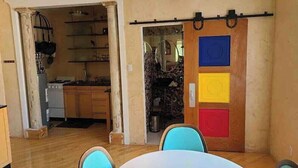 Een kamer met een eettafel, stoelen, een keukenhoek en een kleurrijke schuifdeur.