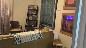 A room with a ceiling fan, a sofa, a chair, a small table, a bookshelf, and framed pictures on the wall.