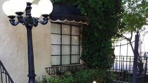 A brick pathway leading to a building with a window covered in ivy, a black metal lamp post, and a green planter with plants. - Comfortable 1BR Condo in Downtown (Fort Worth)