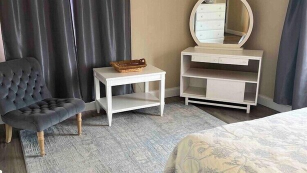 A bedroom with a bed, a chair, a small table, a mirror, and a dresser. - Comfortable 1BR Condo in Downtown (Fort Worth)