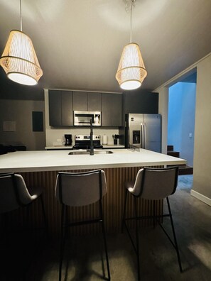 A modern kitchen with a central island, bar stools, stainless steel appliances, and pendant lighting. - Luxury 2-bedroom suite with AC, BBQ, and pool in Pinilla Tamarindo (Pinilla)