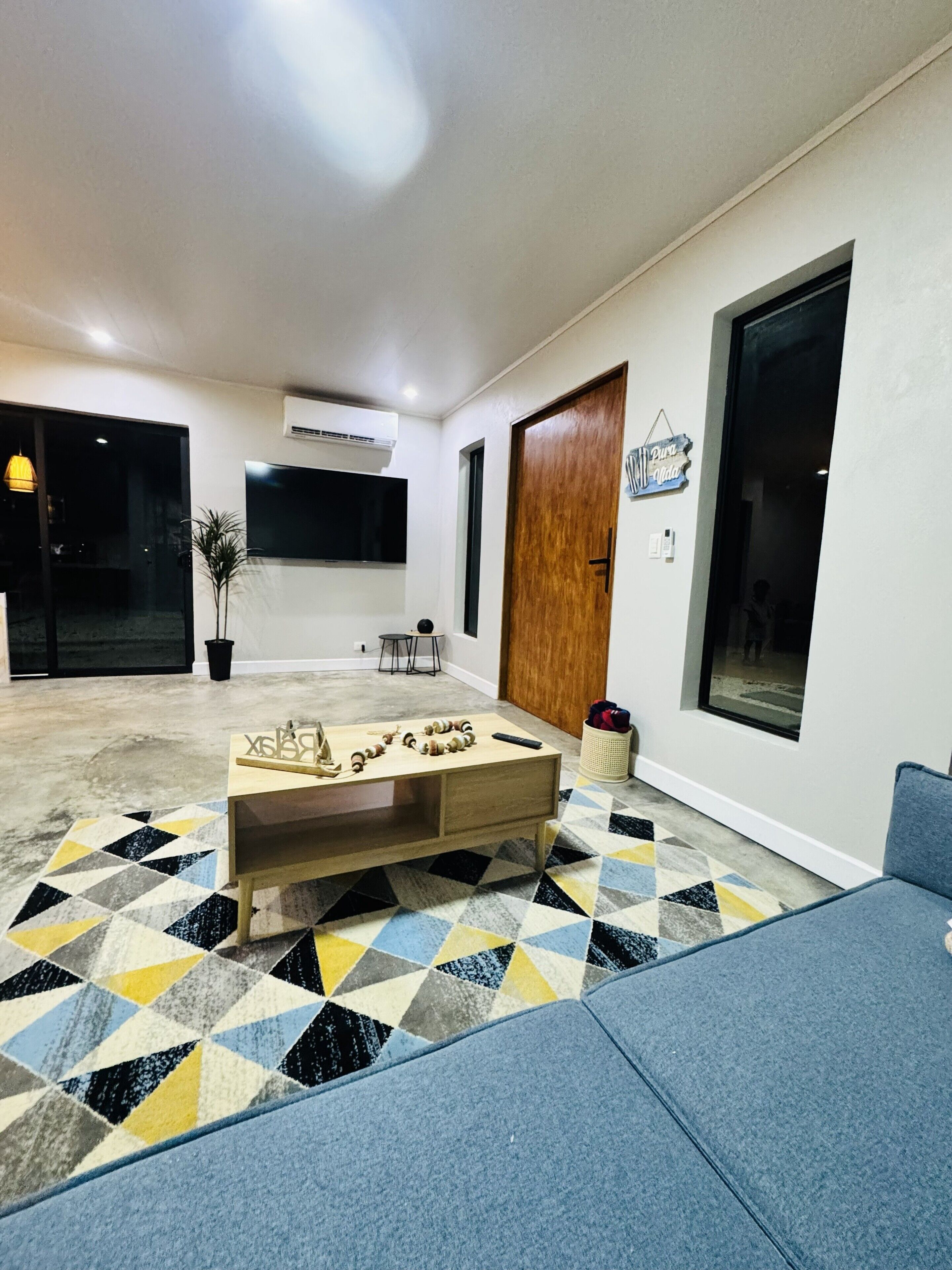 A modern living room with a geometric patterned carpet, a wooden coffee table, and a blue sofa.