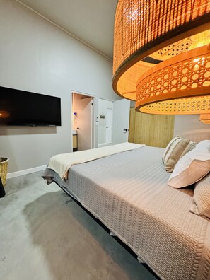 Ein Schlafzimmer mit einem Bett, einem an der Wand montierten Fernseher, einer Tür und einer Hängeleuchte.