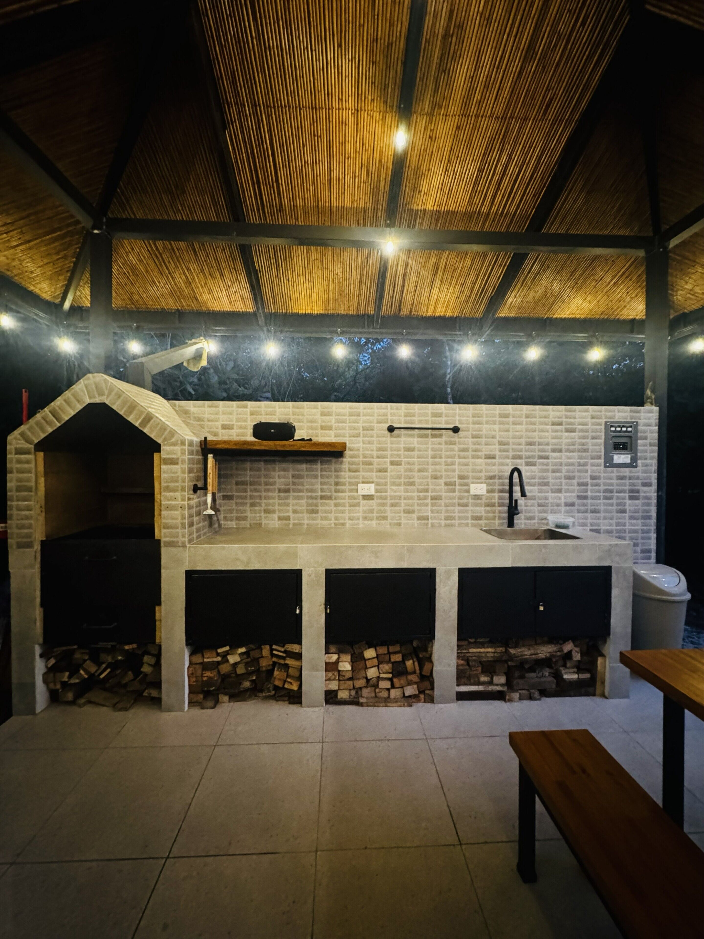 An outdoor kitchen with a brick backsplash, a built-in sink, and a wooden bench.