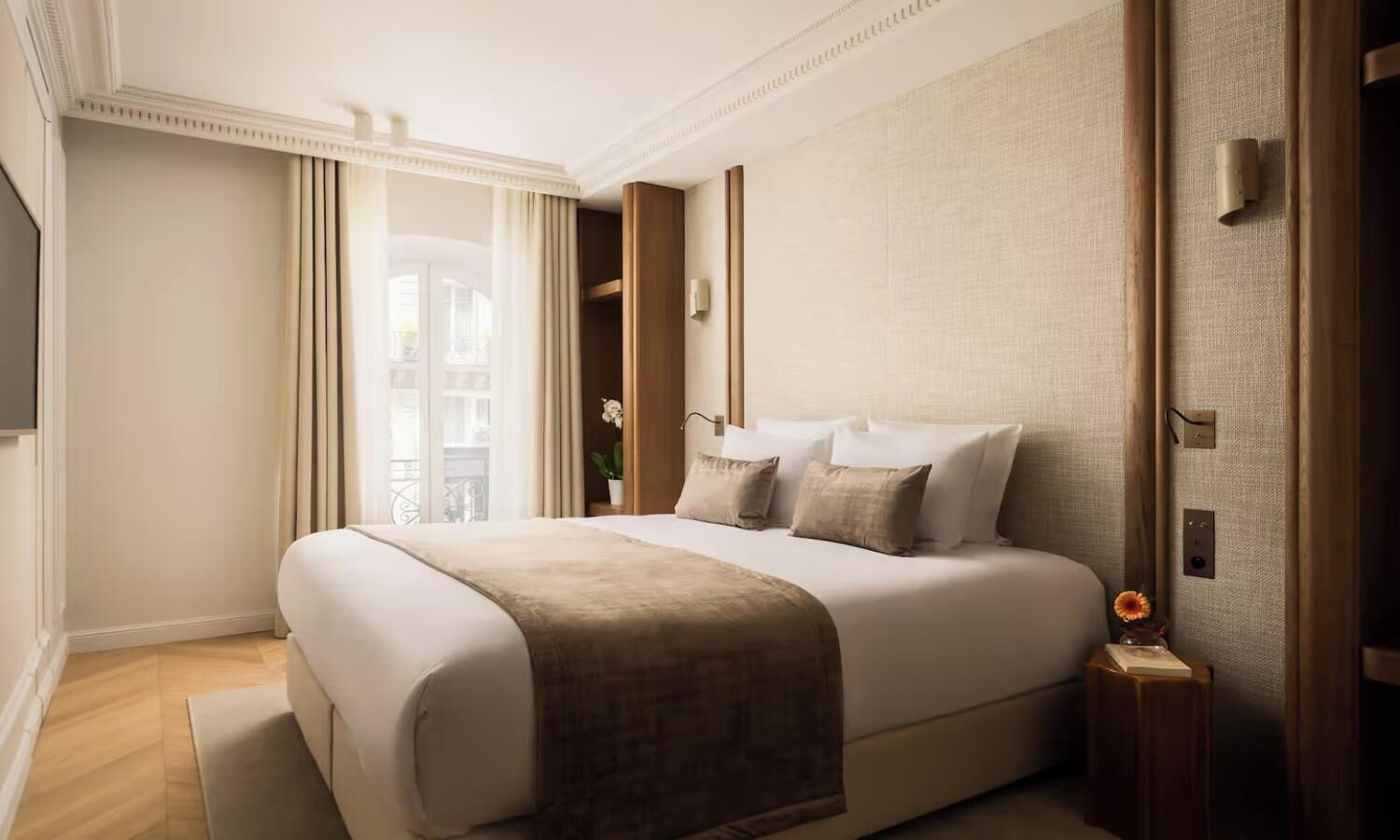 Quarto de hotel com uma cama grande, mesa de cabeceira, cortinas e vista para a cidade.