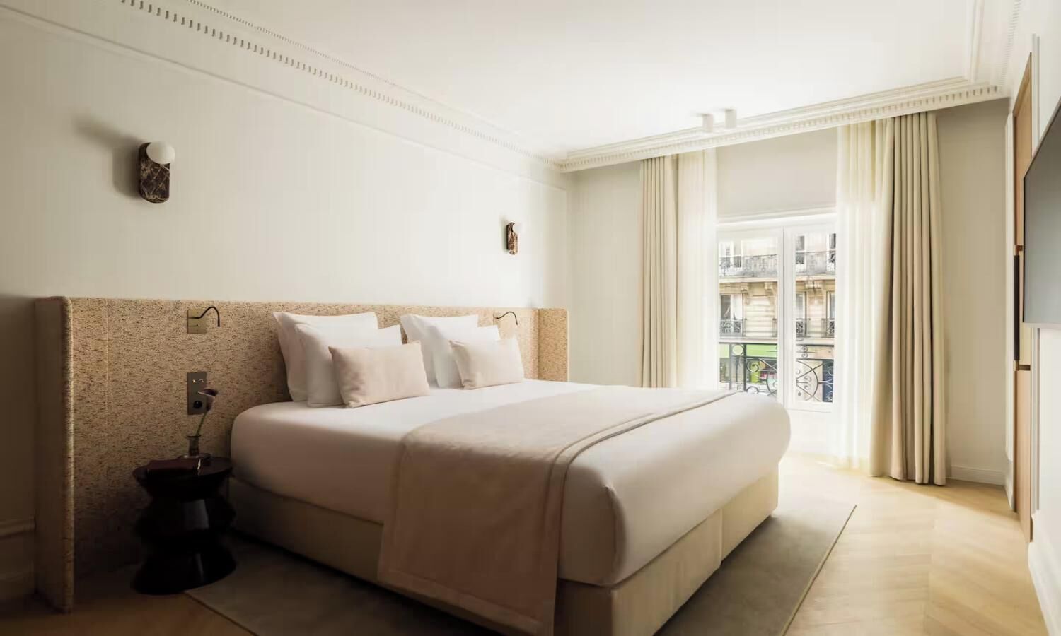 A hotel room with a large bed, a bedside table, a small bedside lamp, and a window with curtains.