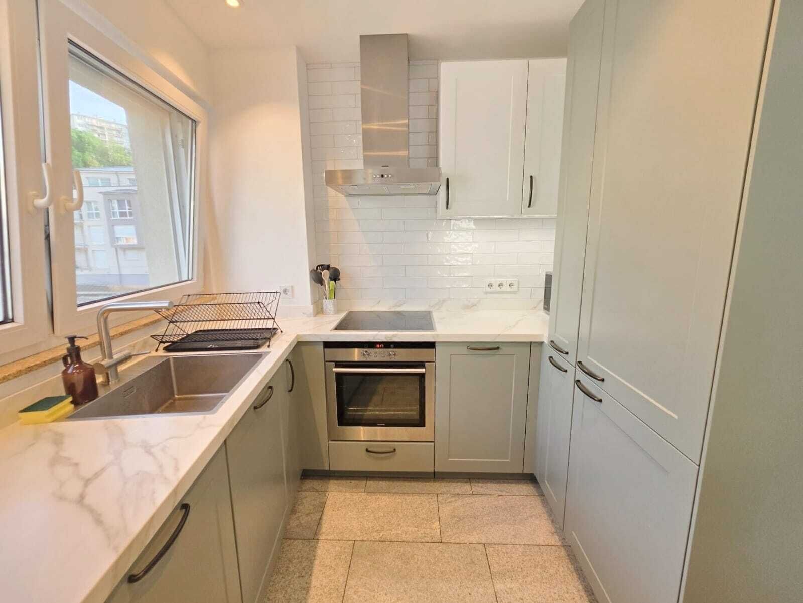 A compact kitchen with a built-in oven, a sink, and a window providing natural light.