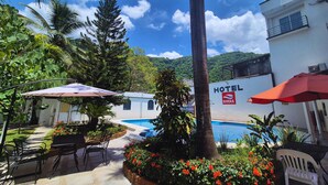 Un hotel con piscina, mobiliario exterior y abundante vegetación.