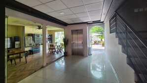 Un vestíbulo de hotel con suelo de baldosas, un mostrador de recepción, un área de descanso con sillas y una mesa, y una escalera.