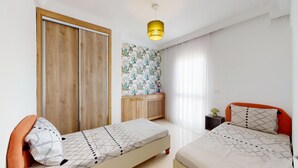 Un dormitorio con dos camas, un armario, un aparador y una lámpara colgante.