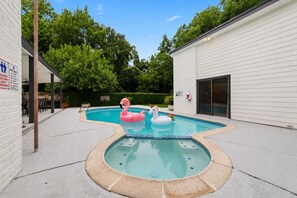 Ein Swimmingpool mit zwei aufblasbaren Flamingos und einem Einhorn-Schwimmpferd, umgeben von einem weißen Gebäude und Grünflächen.