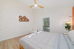 Ein Schlafzimmer mit einem Bett, einem Deckenventilator, einem Fenster mit Jalousien, einem Nachttisch mit Lampe und einer Wanddekoration.