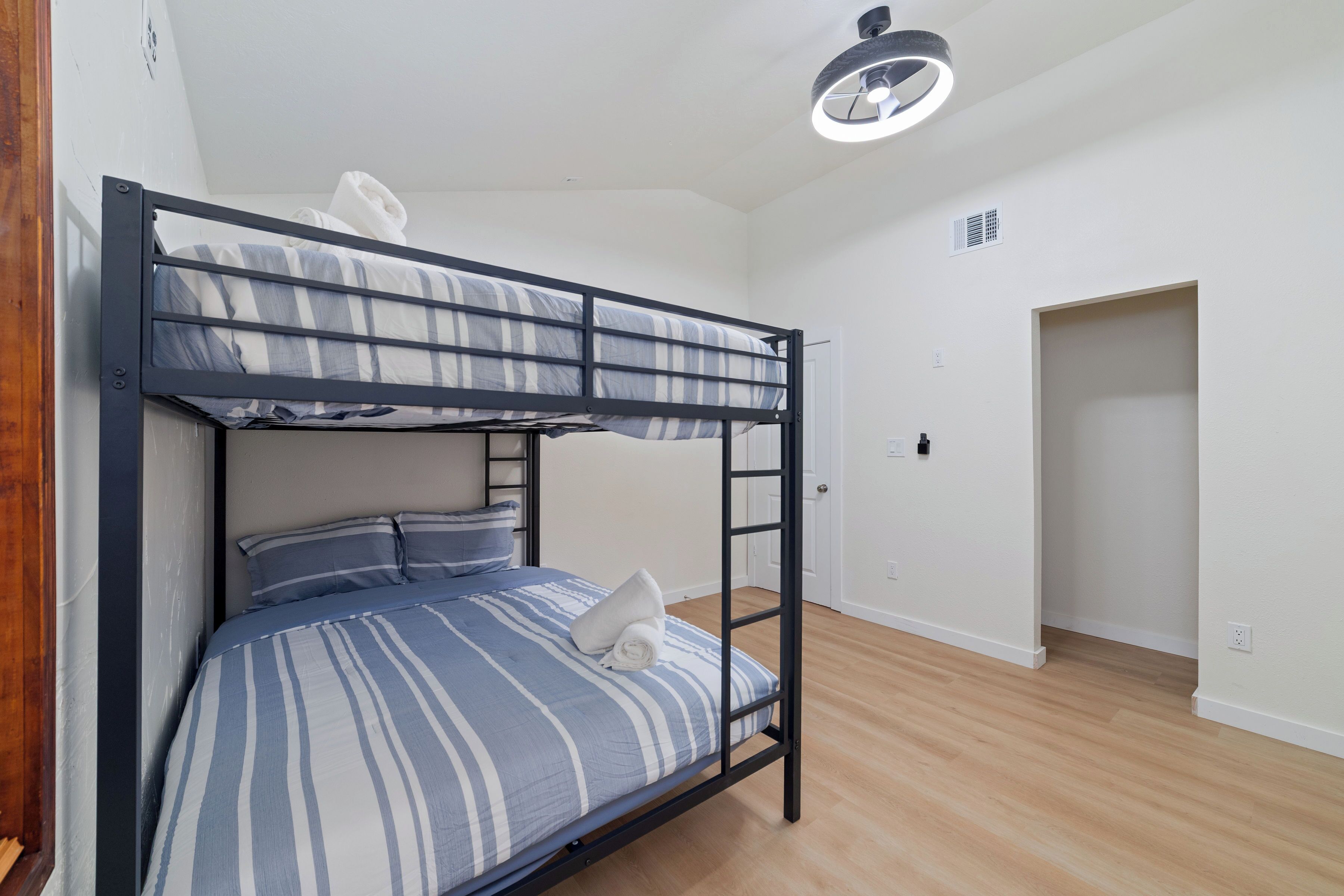 A bunk bed with striped bedding and a white pillow, a ceiling light fixture, and a door leading to another room.