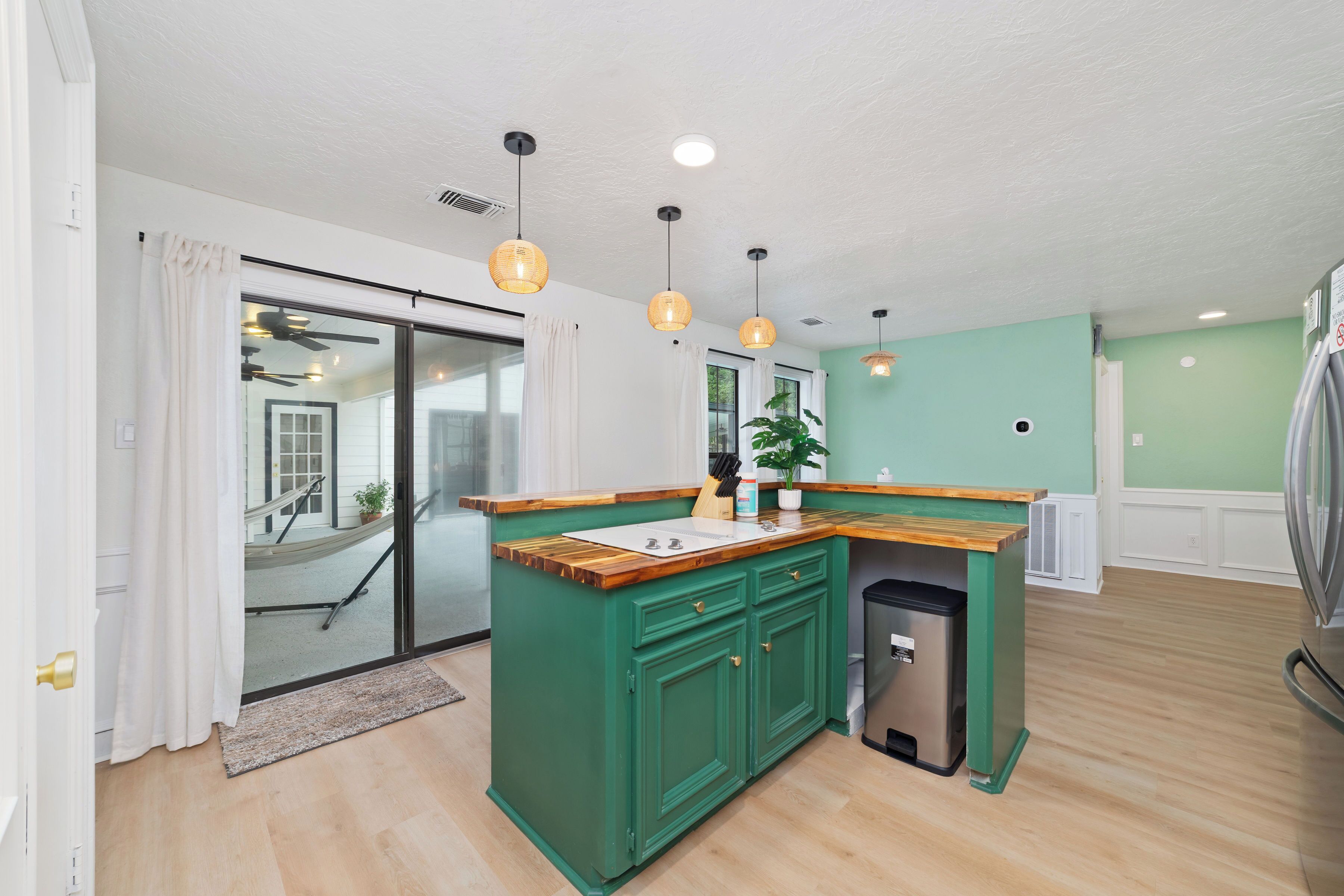 A modern kitchen with green cabinetry, a wooden countertop, and pendant lighting.