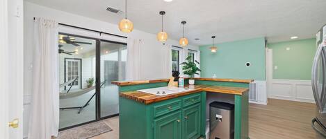 A modern kitchen with green cabinetry, a wooden countertop, and pendant lighting.