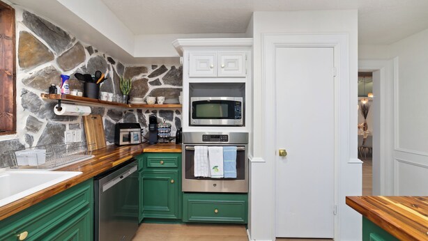 A kitchen with green cabinets, a stone accent wall, a microwave, an oven, and a coffee machine. - Lara Retreat- 6B/4.5 BT- Private Pool and Paris- Game room (Houston)
