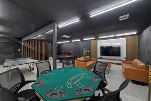 A room with a pool table, a green felt blackjack table, a billiards table, a television, and a sofa. - Lara Retreat- 6B/4.5 BT- Private Pool and Paris- Game room (Houston)