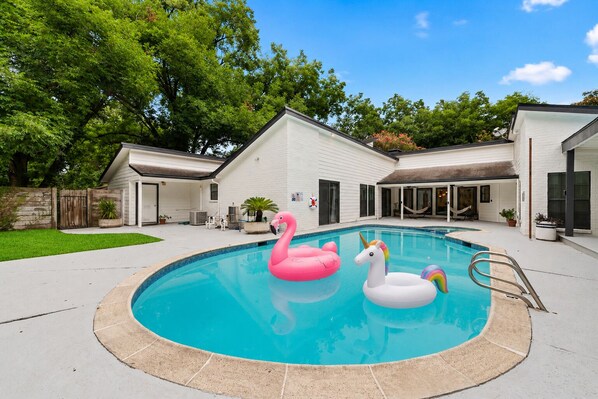 Een achtertuin met een zwembad, twee opblaasflamingo's en een wit huis.
