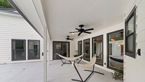A covered outdoor area with two ceiling fans, a hammock, and a patio with large windows. - Lara Retreat- 6B/4.5 BT- Private Pool and Paris- Game room (Houston)