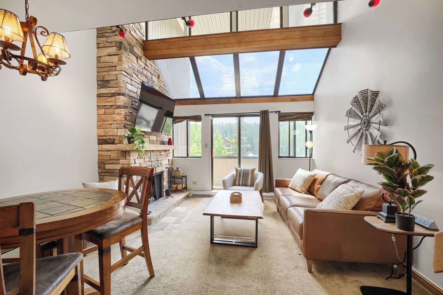 A spacious living room with a stone fireplace, a large window, and a modern chandelier.