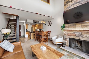 A modern living room with a wooden coffee table, a sofa, a fireplace, and a dining area with chairs and a table. - Freshly Updated Ski-In Ski-Out 2BR Beaver Run (Breckenridge)