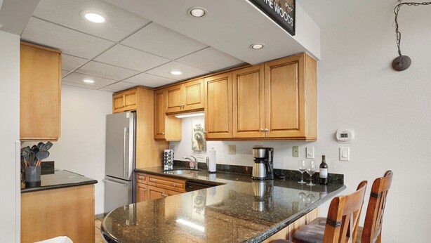A kitchen with wooden cabinets, a granite countertop, a refrigerator, a coffee maker, and bar stools. - Freshly Updated Ski-In Ski-Out 2BR Beaver Run (Breckenridge)